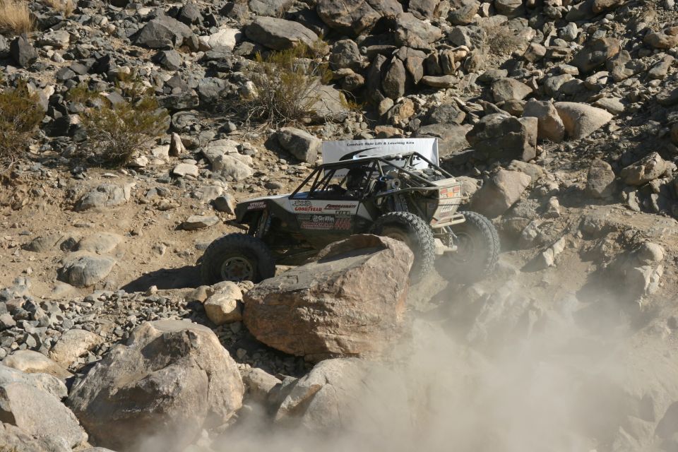 Custom off-road buggy with roll cage navigating rocky terrain, kicking up dust