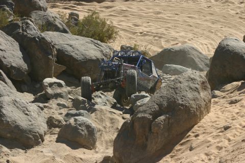 1992 Jeep Wrangler - An off-road buggy navigates a challenging rocky terrain with sand dunes in the background.