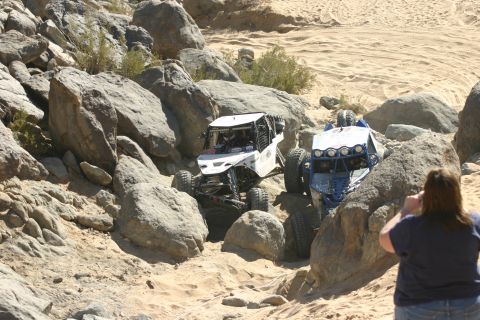 1992 Jeep Wrangler - Two off-road vehicles tackle a challenging rocky course, with a spectator observing the action.