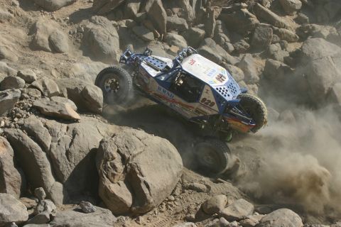 1992 Jeep Wrangler - A custom off-road buggy navigates a challenging rocky terrain, kicking up dust as it goes.