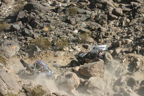 1992 Jeep Wrangler - Two custom off-road vehicles tackle a challenging rocky course, kicking up dust.