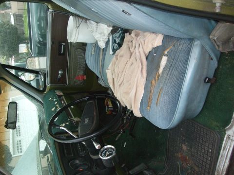 1979 Ford Bronco - The interior of a vehicle shows a blue bench seat with a towel and bucket, and a steering wheel.