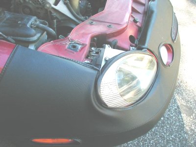 1997 Ford Taurus - The front of a car is shown, with a headlight and engine components visible beneath a black car bra.