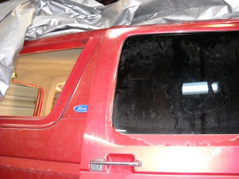 1993 Ford C-150 (Centurion Conversions) - A red Ford truck is partially covered by a tarp, revealing its side profile and a blue Ford emblem.