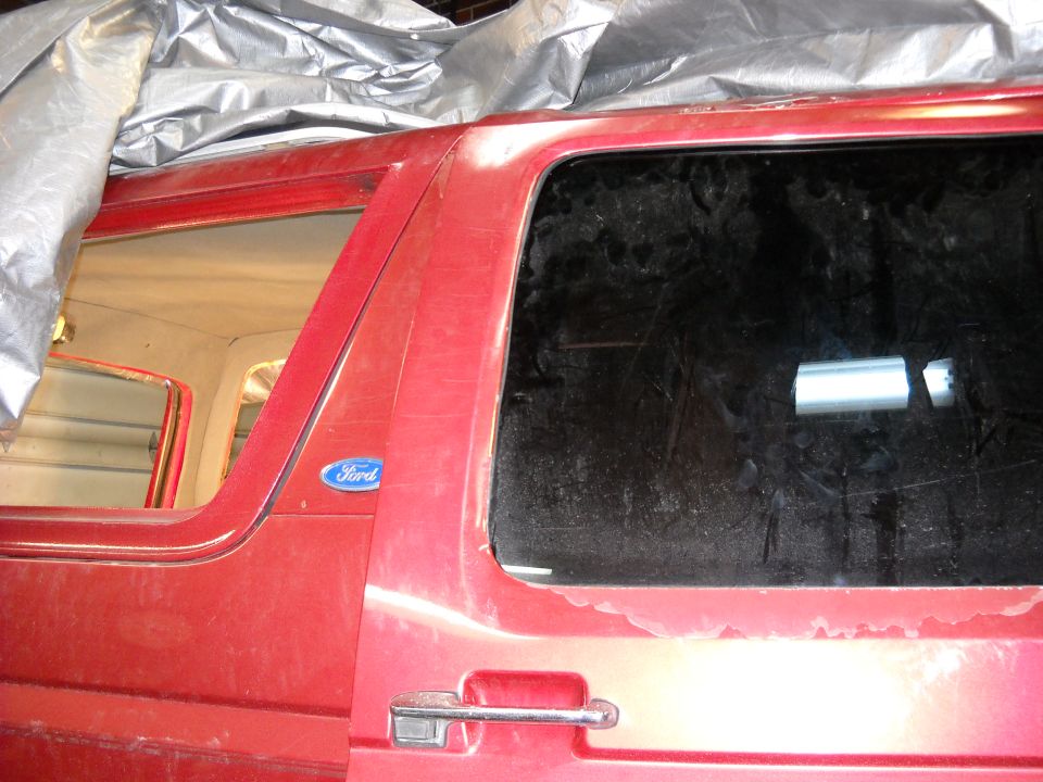 Side view of a red Ford truck with a tarp over the roof. Shows the door handle and Ford emblem