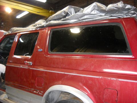 1993 Ford C-150 (Centurion Conversions) - Red SUV with tarp on roof, seen from the side in a garage. Year is likely 1992 based on body style.