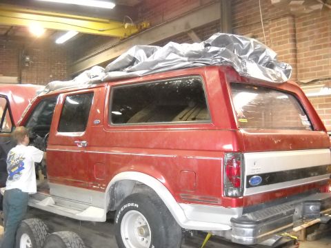 1993 Ford C-150 (Centurion Conversions) - A person works on the interior of a red Ford Bronco, which is covered by a tarp.