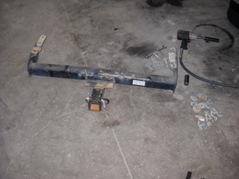 1993 Ford C-150 (Centurion Conversions) - A trailer hitch assembly lies on a garage floor next to an impact wrench and various bolts and brackets.