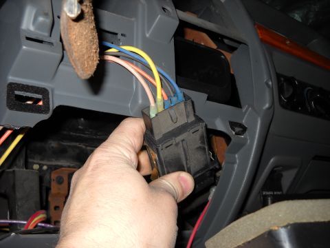 1993 Ford C-150 (Centurion Conversions) - A hand disconnects a wiring harness from the steering column area of a vehicle's dashboard.