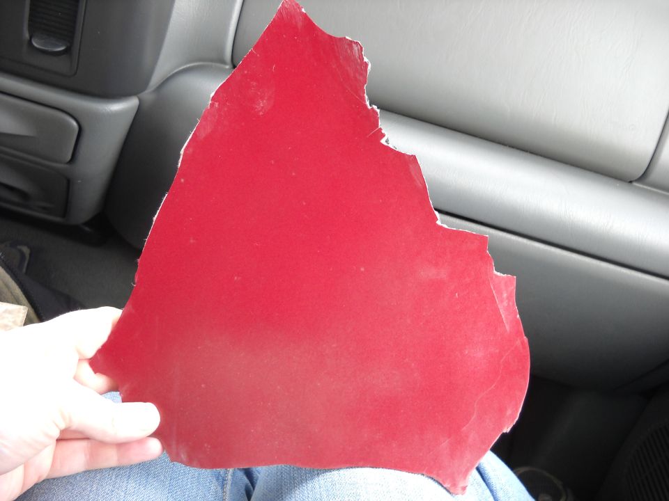 Hand holding a torn piece of red trim inside a vehicle. Interior dash visible