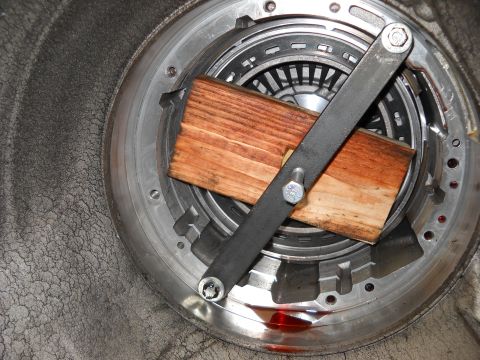 1993 Ford C-150 (Centurion Conversions) - Close-up of a transmission's internal components, including a torque converter clutch assembly held by wooden blocks and a metal tool.
