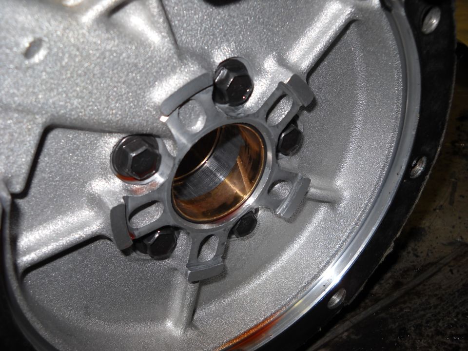 Close-up of a transmission torque converter housing with a bronze bushing and six bolts