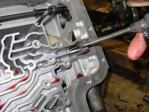 1993 Ford C-150 (Centurion Conversions) - Close-up of an automatic transmission valve body with a tool being used to clear a passage.