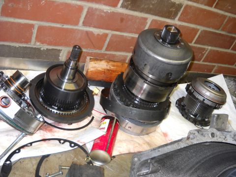 1993 Ford C-150 (Centurion Conversions) - Various parts of an automatic transmission are spread out on a workbench, ready for inspection or repair.