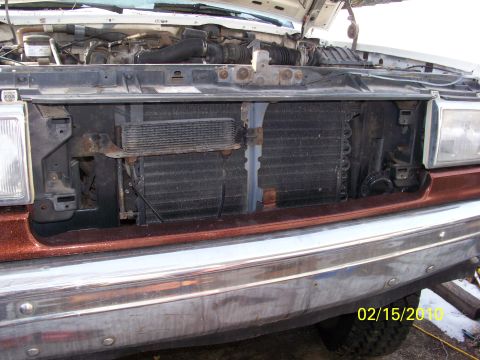 1989 Ford Bronco - The front grille and radiator of a truck are visible with the hood open, revealing engine parts.