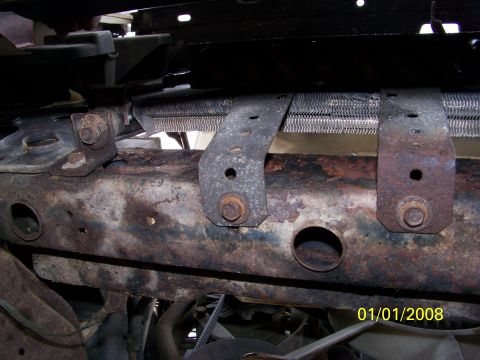 1989 Ford Bronco - Close-up of a rusted vehicle frame showing the radiator mounting brackets and part of the radiator.