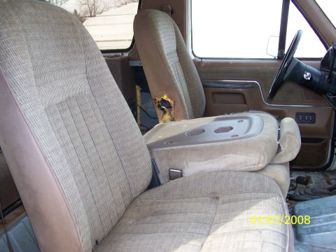 1989 Ford Bronco - Interior view of a vehicle with worn tan seats and a center console, showing signs of age and damage.