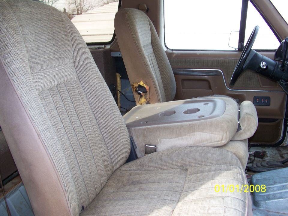 Tan fabric seats with vertical stitching and a torn driver's seat cushion. Center console and dashboard are visible