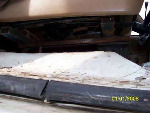 1989 Ford Bronco - Close-up view of the seat mounting hardware and floor panel inside a vehicle.