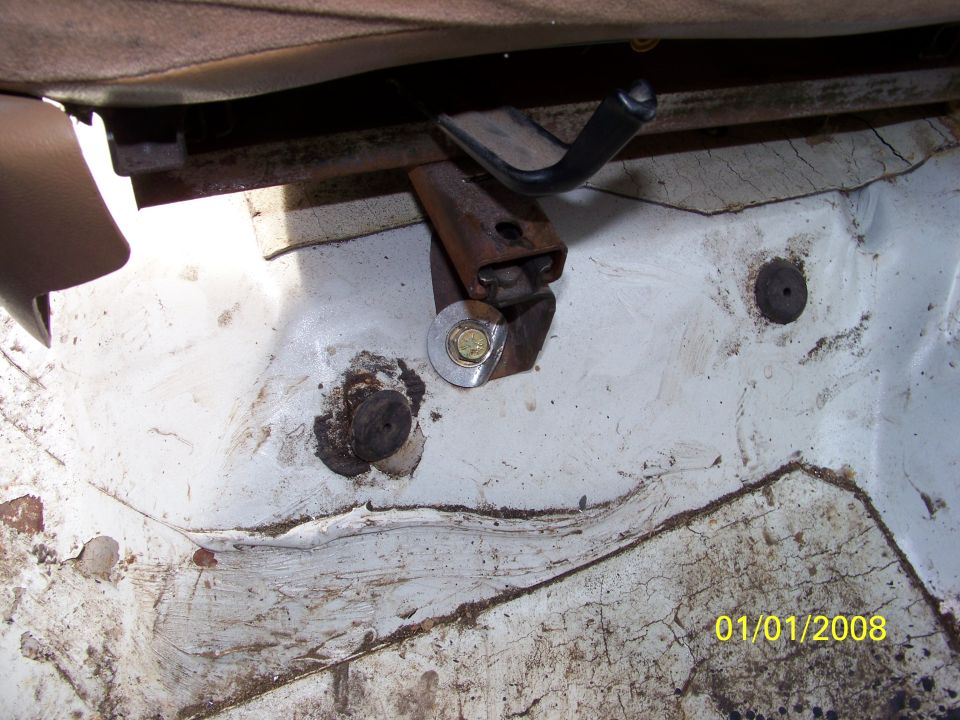 Close-up of a rusty seat mounting bracket and bolt on a white floor