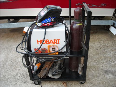 1979 Ford F-150 - A cart holds welding equipment including a Hobart welder, gas cylinder, helmet, gloves, and grinder.