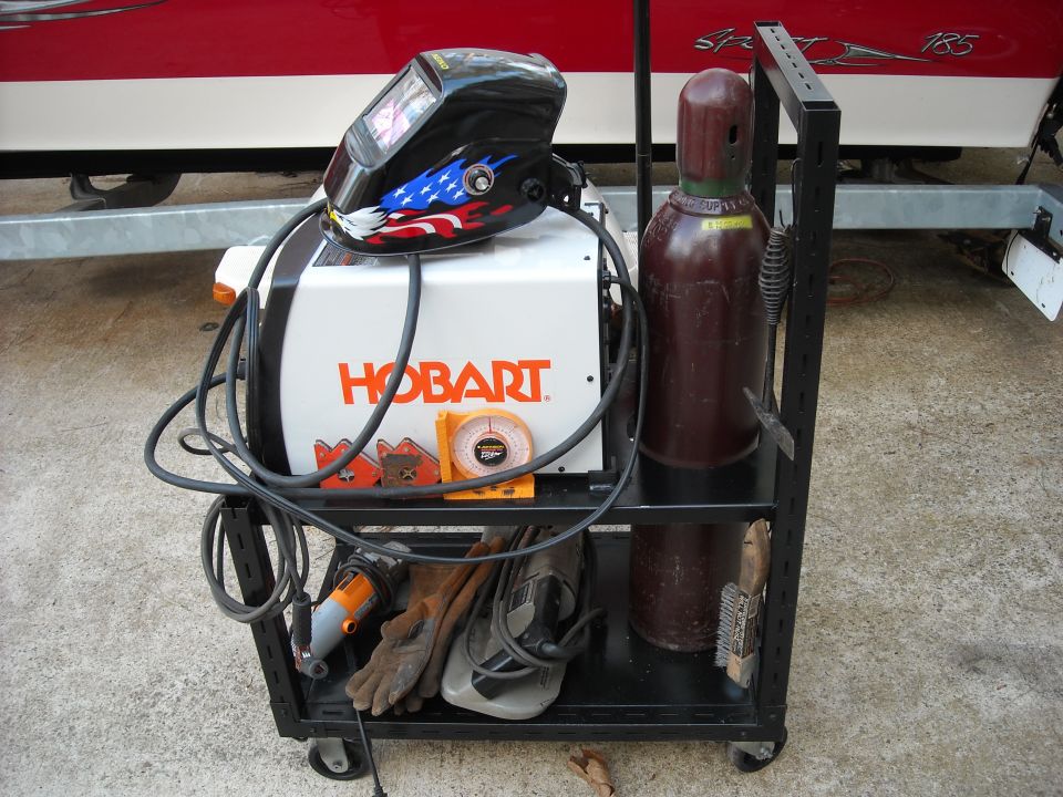 Welding cart with Hobart welder, gas cylinder, helmet, gloves, and grinder