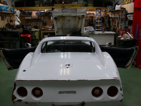 1976 Chevrolet Corvette - The rear of a white 1976 Chevrolet Corvette is shown with its doors open and hood raised, revealing a workshop environment.