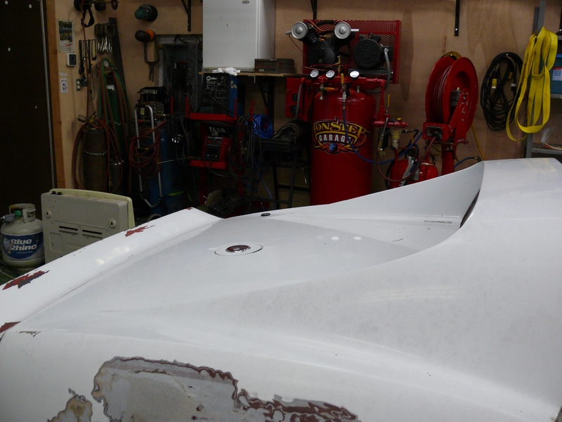 white car hood with primer showing in a garage with tools and an air compressor