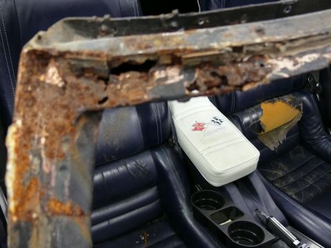 1976 Chevrolet Corvette - The interior of a 1976 Chevrolet Corvette shows a heavily rusted metal frame in the foreground, with the car's seats and center console vis…