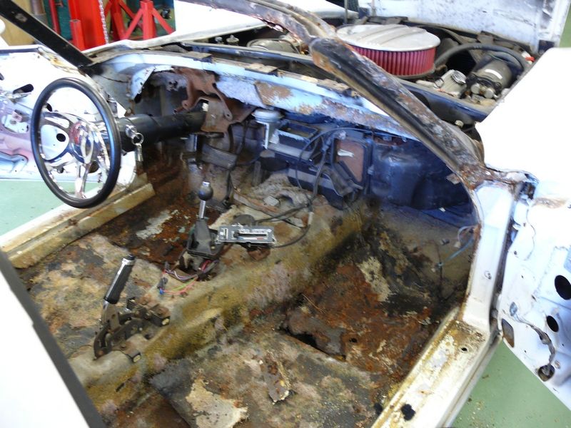 Car interior with extensive rust damage, missing dashboard components, and exposed wiring
