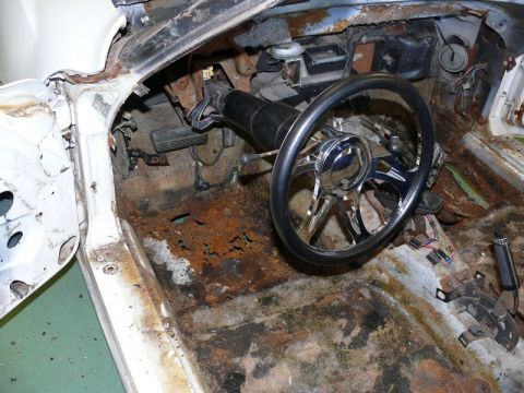 1976 Chevrolet Corvette - The interior of a car shows severe rust damage, with the steering wheel and pedals visible.