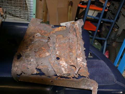 1976 Chevrolet Corvette - A severely corroded metal piece is shown, likely a car part, on a dark blue surface.