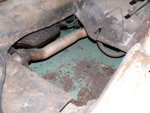 1976 Chevrolet Corvette - Underbody/floor pan view showing a rusted metal chassis area with an exhaust pipe running through it, exposed teal/green painted floor, and…