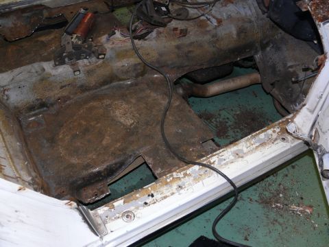 1976 Chevrolet Corvette - Interior floor pan of a car stripped down for restoration, showing heavy surface rust and corrosion on the transmission tunnel and floor, w…