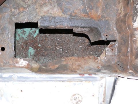 1976 Chevrolet Corvette - Close-up of a heavily rusted metal floor pan or body panel with a large cut-out opening exposing corroded surfaces, some green primer and b…