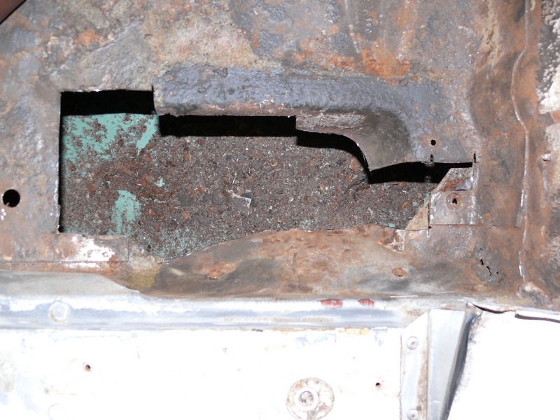 Rusted vehicle floor pan with cut-out opening and green primer remnants