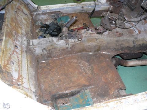 1976 Chevrolet Corvette - Stripped interior floor pan of a car showing heavy surface rust, exposed sheet metal, and remaining components including a shifter mechanis…