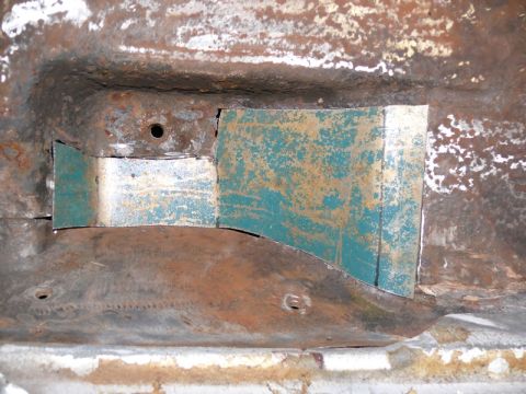 1976 Chevrolet Corvette - Close-up of a rusty sheet-metal repair area on a vehicle underbody or frame, with a teal and yellow patch panel welded in over corroded met…