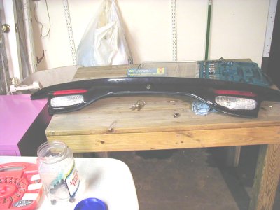 1997 Ford Taurus - A car's rear spoiler with integrated brake lights is disassembled on a workbench.