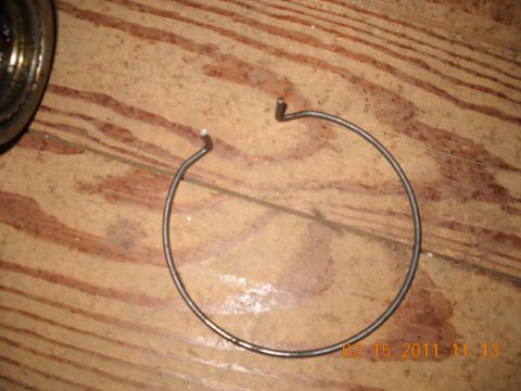 1982 Ford Bronco - A snap ring is shown on a wooden surface, with a portion of another component to its left.