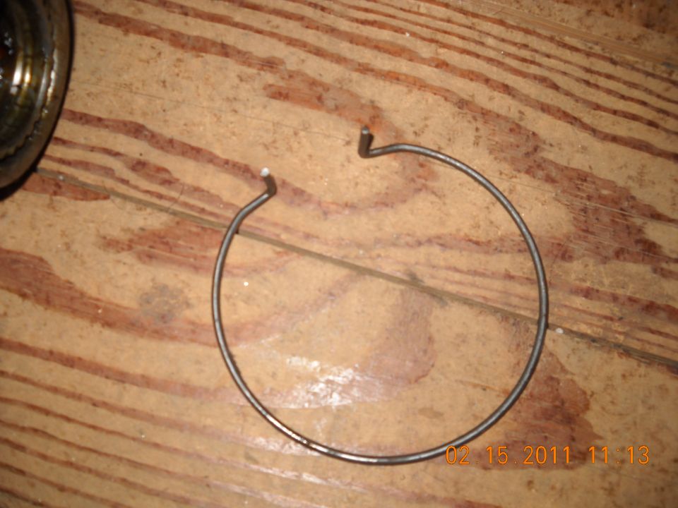 Metal snap ring on a wood surface. Part of a larger assembly is visible to the left