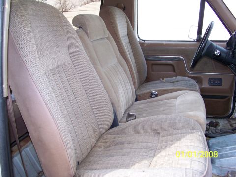 1989 Ford Bronco - The interior of a vehicle shows tan fabric bench seats and a door panel, with visible watermarks.