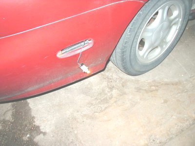 1997 Ford Taurus - Low-angle close-up of the red rear quarter panel and door of a sedan, showing a chrome-trimmed pull-up door handle with a small wire or cli…