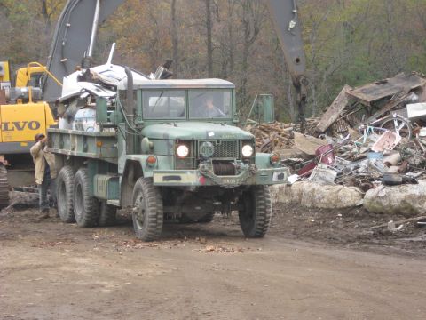 1985 Chevrolet Blazer - A military dump truck is being loaded with scrap metal at a junkyard, with an excavator visible.
