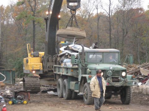 1985 Chevrolet Blazer - A man stands by a green military truck as a crane lifts debris into its bed at a scrap yard.