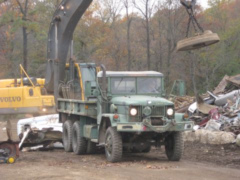 1985 Chevrolet Blazer - A large green military truck is at a junkyard, with an excavator and a magnetic crane nearby.