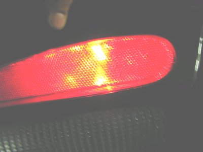 1997 Ford Taurus - A person's finger is visible above a red third brake light, with yellow bulbs illuminated within.