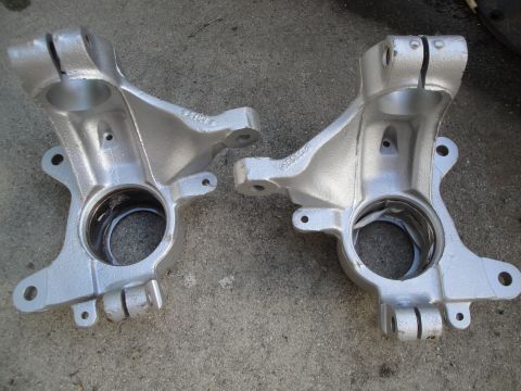 1993 Ford Taurus - A pair of steering knuckles, one with a visible crack, sit on a concrete surface.