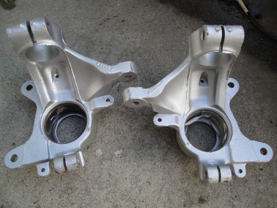 Pair of silver painted steering knuckles on concrete. Part numbers are visible