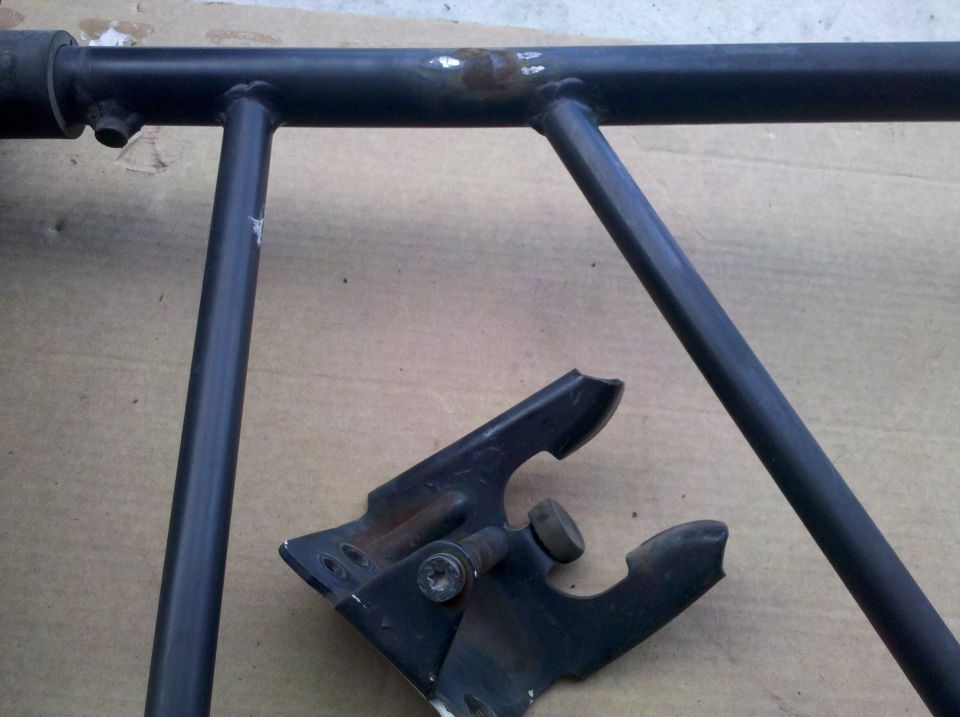 Black tube spare tire carrier frame with stamped-steel latch bracket on cardboard